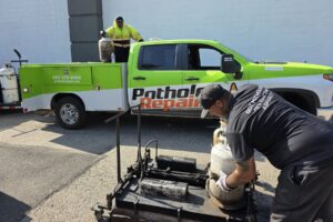 PotholeRepair.com crew setting up the infrared heater beside the branded service truck in a commercial parking lot before a permanent thermal pothole repair