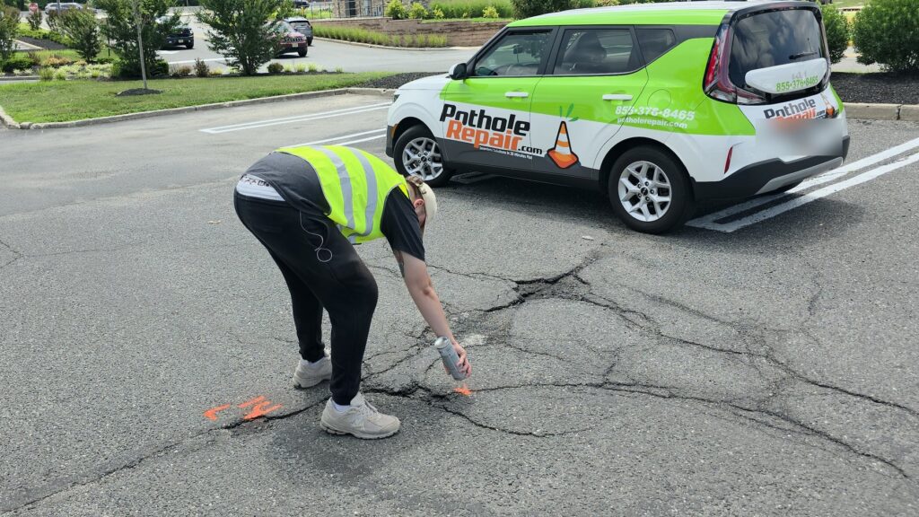 PotholeRepair.com technician spray-marking a pothole for repair in a commercial parking lot beside the branded PotholeRepair.com service vehicle